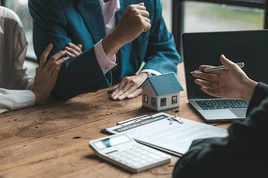 Three people discussing with a miniature house, calculator, and a contract agreement on the table