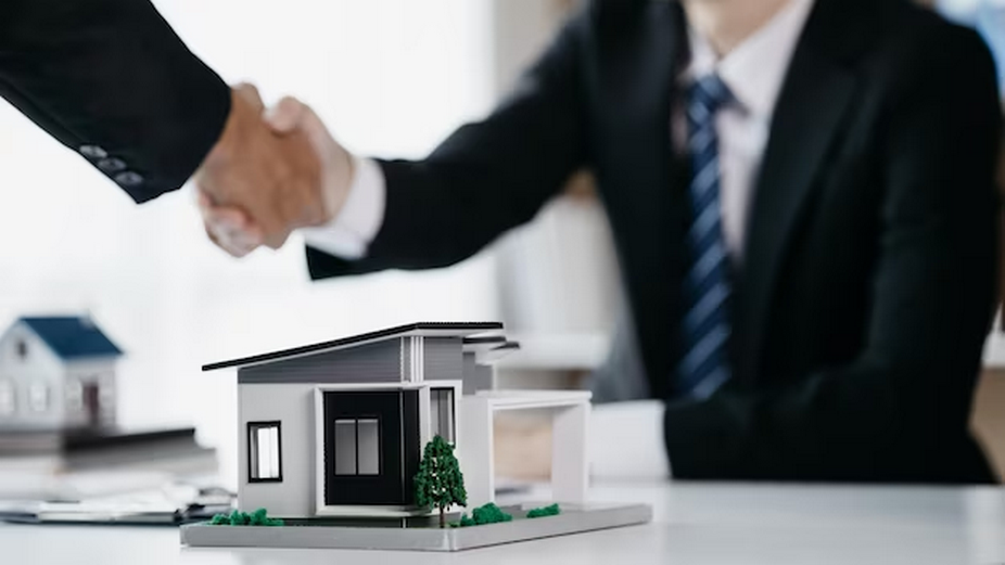 Two people shaking hands with a miniature house on the table